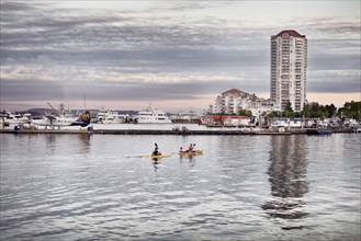Scenery of people kayaking at Nanaimo city waterfront in the evening with the harbour and the city skyline at back