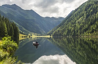 Fisherman on Lake Riesachsee with reflection of forest and mountains