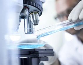Chemist studying blue liquid under microscope