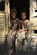 Two local children sitting in front of a hut