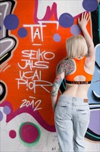 Young blond tattoo model posing at graffiti wall