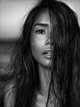 Sensual black and white beauty portrait of a young woman exotic mixed-race ethnicity face with long dark hair and sand particles on her hair and skin