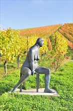 Seated bronze sculpture by Karl Ulrich Nuss in front of vineyards in autumn