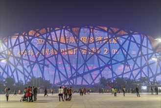 People on square in front of illuminated National Stadium in the Olympic Park