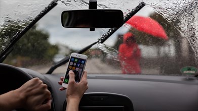 Woman sitting at the wheel of a car playing with mobile phone in rain