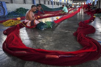 Local men repairing fishing nets in hall at harbour