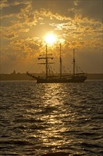 Three-masted sailing ship in front of sunset