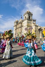 Women in traditional dresses with flower baskets dancing on the main square Zocalo in front of church Santo Domingo de Guzman