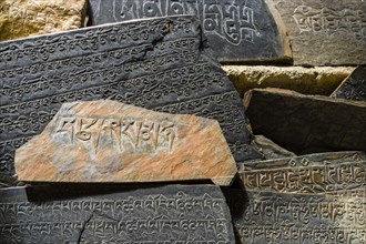 Mani stones with the engraved tibetan mantra Om Mani Padme Hum are piled up to a wall