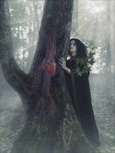 Woman druid in the forest listening to the heartbeat of a tree
