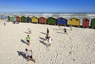 Teenagers play rugby in front of colourful beach houses