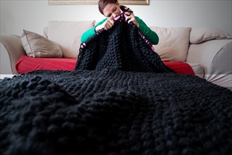 Woman knitting a blanket with large knitting needles