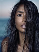 Sensual beauty portrait of a young asian woman with long wet dark hair full of sand particles covering her face