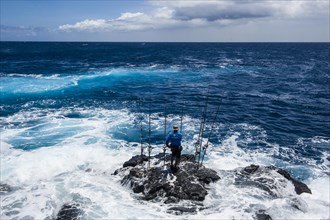 Fisherman standing on a rock in The Sea with his angling rods
