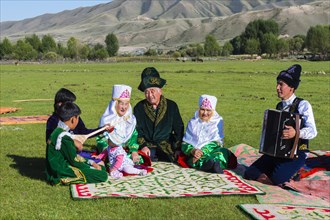 Kazakh family in traditional clothes listening to the music of an accordion player