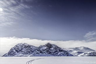 Driving tracks head off across a frozen fjord towards distant mountains