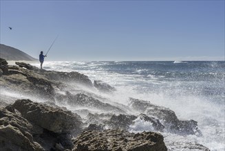 Angler standing on rocky coast with strong surf