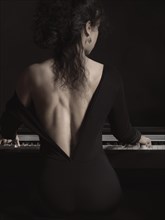 Young woman in a black dress with a low back cut playing the piano