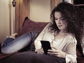 Young woman lying an a sofa holding an Apple iPhone 7 Plus