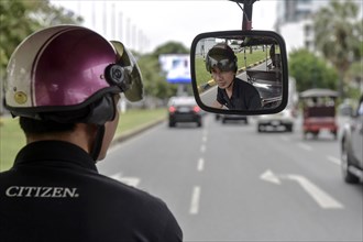 Tuk tuk driver with helmet looking in the rearview mirror