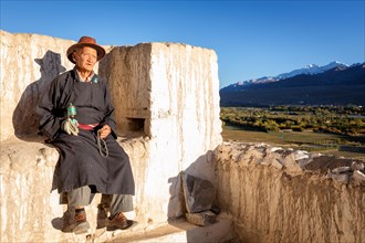 Elderly man with a prayer wheel resting at Spituk Gompa