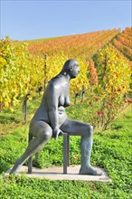 Seated bronze sculpture by Karl Ulrich Nuss in front of vineyards in autumn