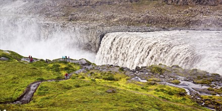 Hikers at the edge of the Dettifoss waterfall with falling water masses