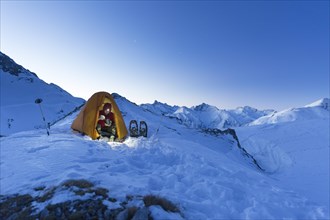 Snowshoe hiker in tent eating in the snow on the Madelejoch