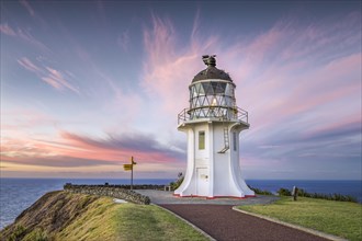Lighthouse with signpost at Cape Reinga at sunset with pink clouds
