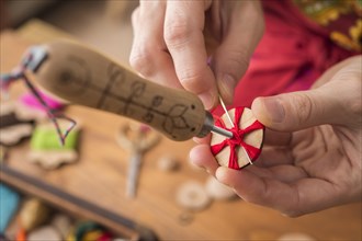 Button maker in third step of Posamentenknopfe production holding wooden blank and vise carefully stitching and wrapping red yarn into star pattern