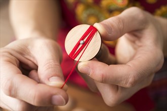 Button maker in the second step of Posamentenknopfe production holding wooden blank and carefully wrapping red yarn