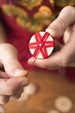 Button maker in third step of Posamentenknopfe production holding wooden blank with vise and carefully wrapping red yarn in star pattern