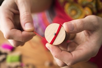 Button maker holding wooden blank and wrapping red yarn