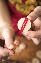 Button maker in the second step of Posamentenknopfe production holding wooden blank and carefully wrapping red yarn