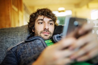 Young man lies relaxed with smartphone on sofa