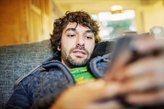 Young man lies relaxed with smartphone on sofa