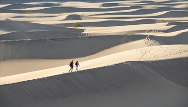 Two people walking on sand dunes