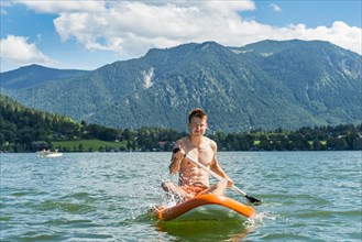 Young man sitting on a paddle board on Lake Schliersee