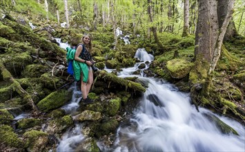Hiker beside stream flowing through forest