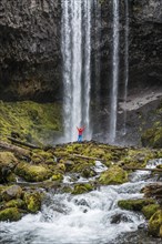 Hiker with raised arms in front of a high waterfall
