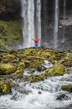 Hiker with raised arms in front of a high waterfall