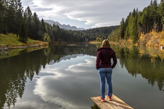 Female hiker stands on a footbridge and looks across the lake