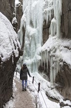 Young woman in the icy Partnachklamm with icicles and snow in winter