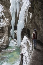 Young woman in the icy Partnachklamm with icicles and snow in winter