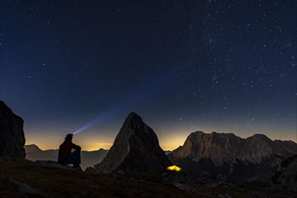 Summit of the Sonnenspitze with mountaineer and tent as well as Zugspitze in the background with blue hour and starry sky