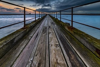 Old wooden jetty in the sea with dramatic clouds at sunset