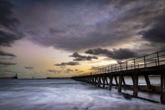 Bridge in the sea with dramatic clouds at sunset