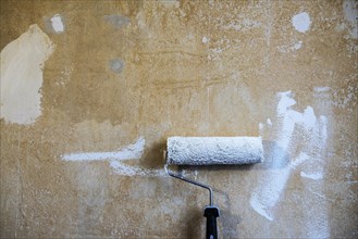 Painter's roller with white paint leaning against a plastered wall