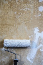 Painter's roller with white paint leaning against a plastered wall