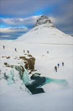 Tourists at the frozen waterfall Kirkjufellsfoss and the mountain Kirkjufell with snow